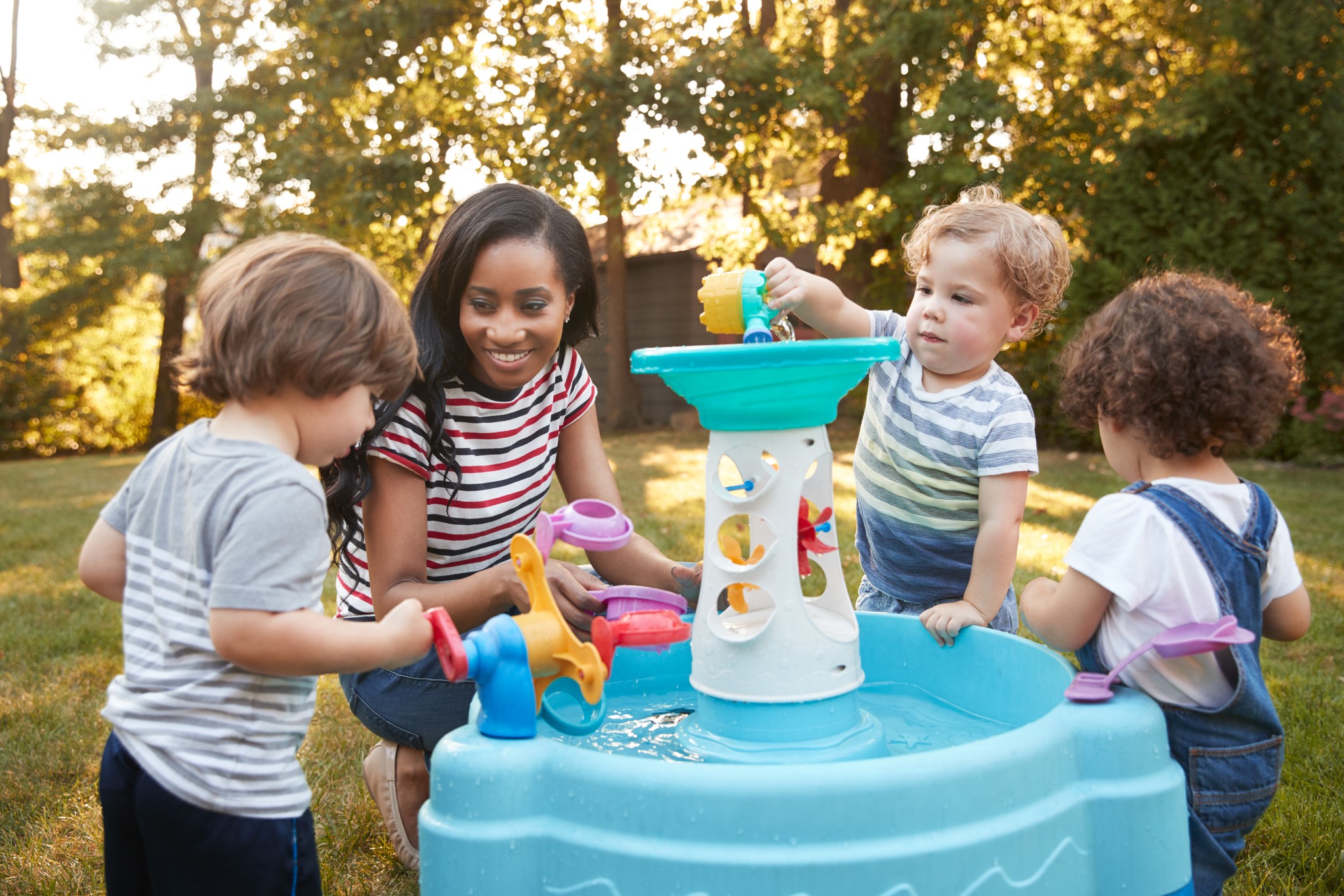 Mother And Young Children Playing With Water Table In Garden